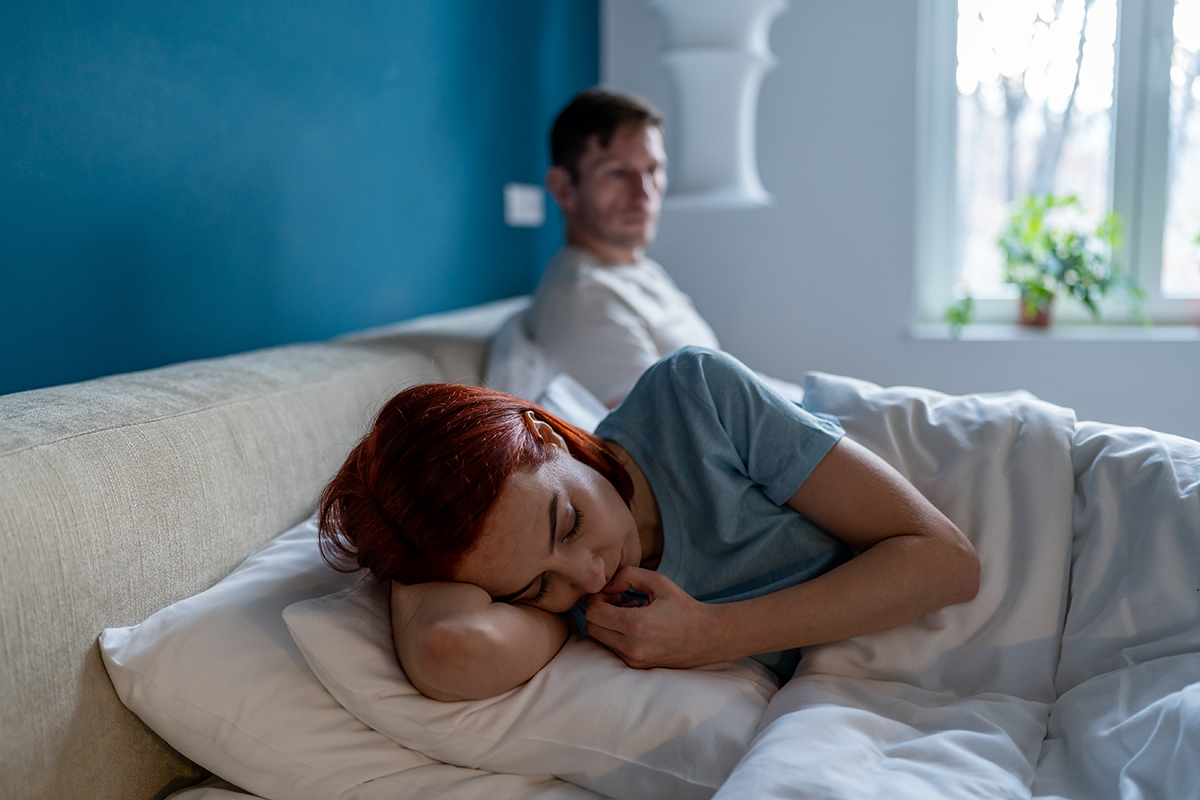 Depressed female lies on edge of bed separated from man husband