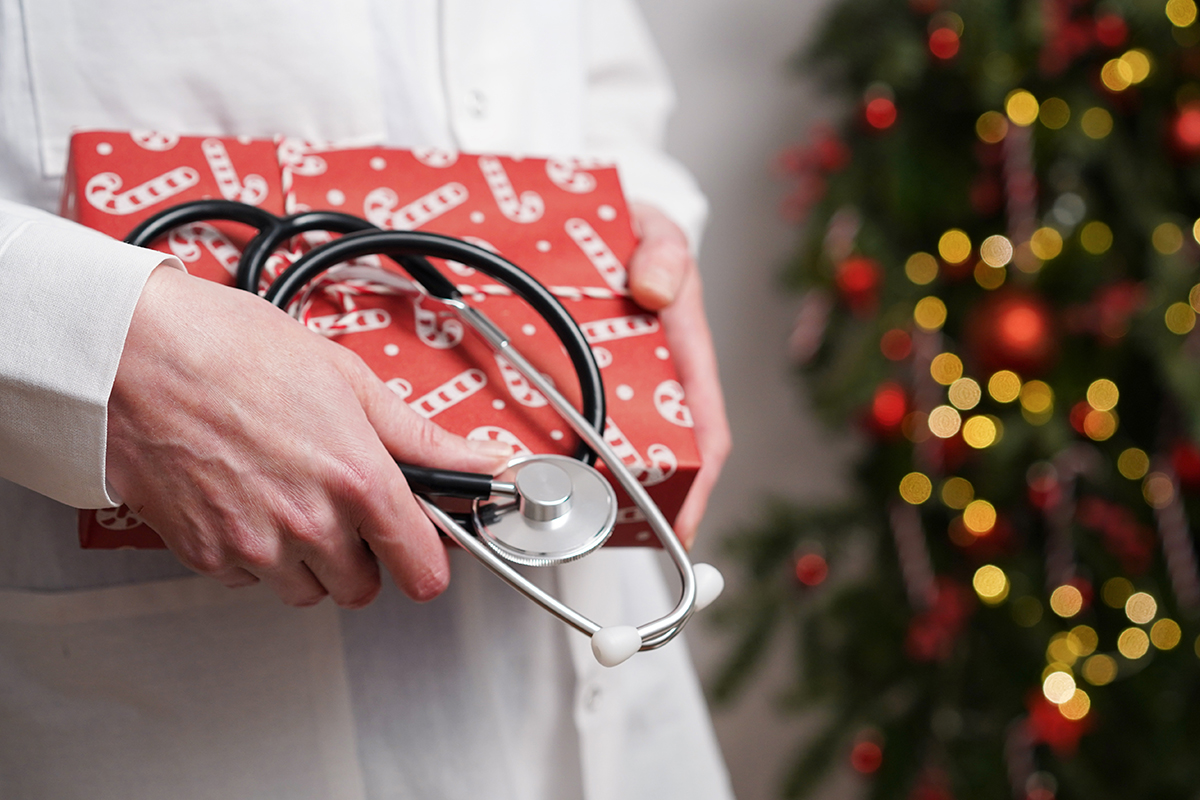 Doctor in white coat holds stethoscope and gift box wrapped in red paper