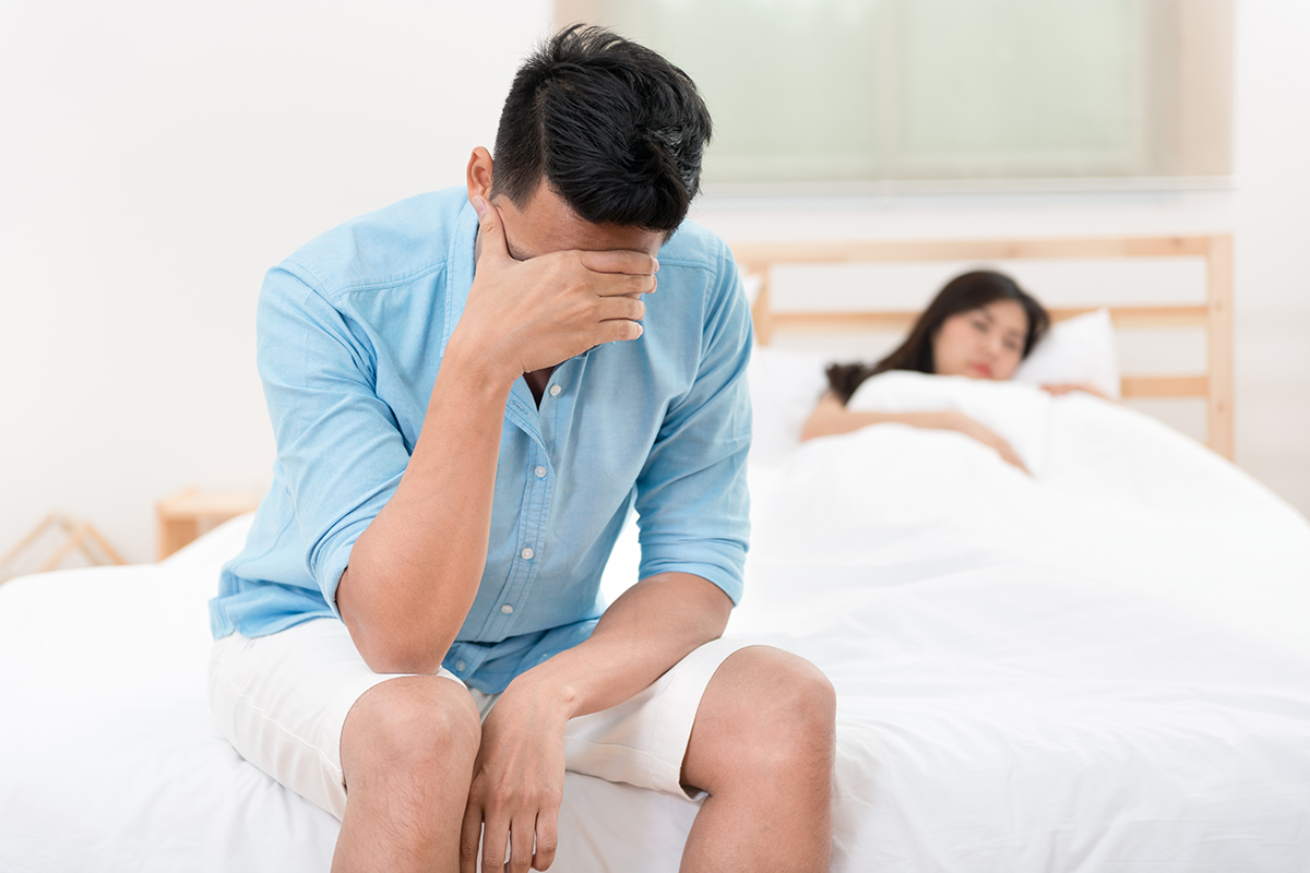 Husband unhappy and disappointed in the erectile dysfunction during sex while his wife sleeping on the bed